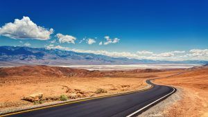 A road in the middle of a desert with mountains in the background.