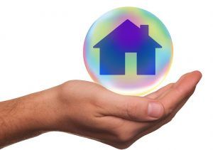 A hand is holding a bubble with a house inside of it.