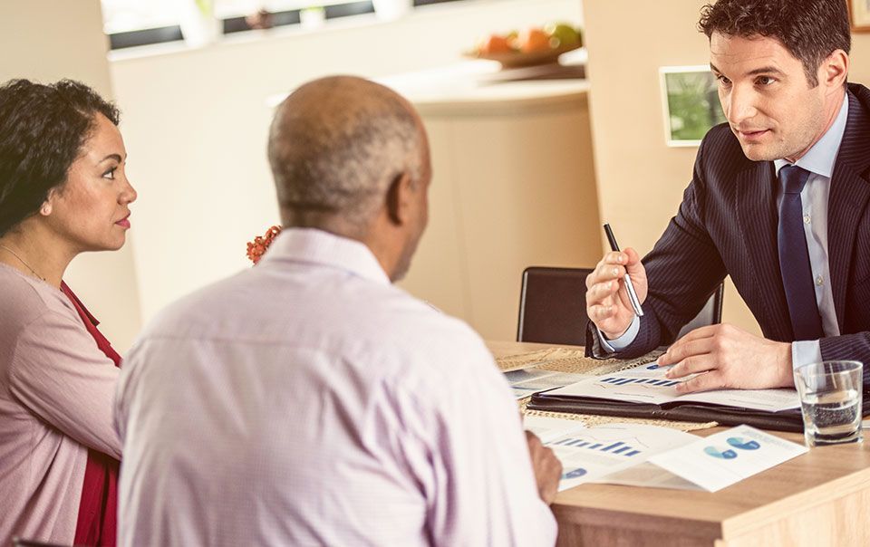 A man in a suit and tie is sitting at a table talking to a man and woman.