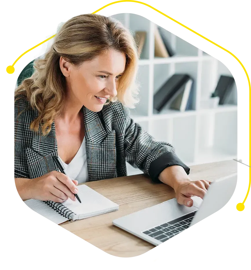 a woman sits at a desk with a notebook and a laptop