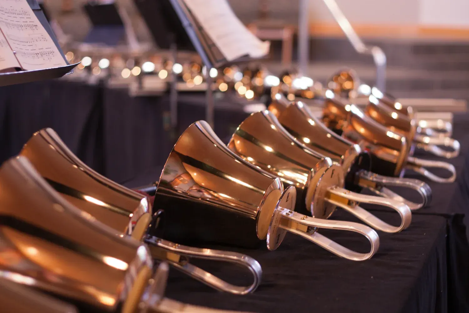 Close-up of a row of gold handbells on a black table with music sheets in the background.