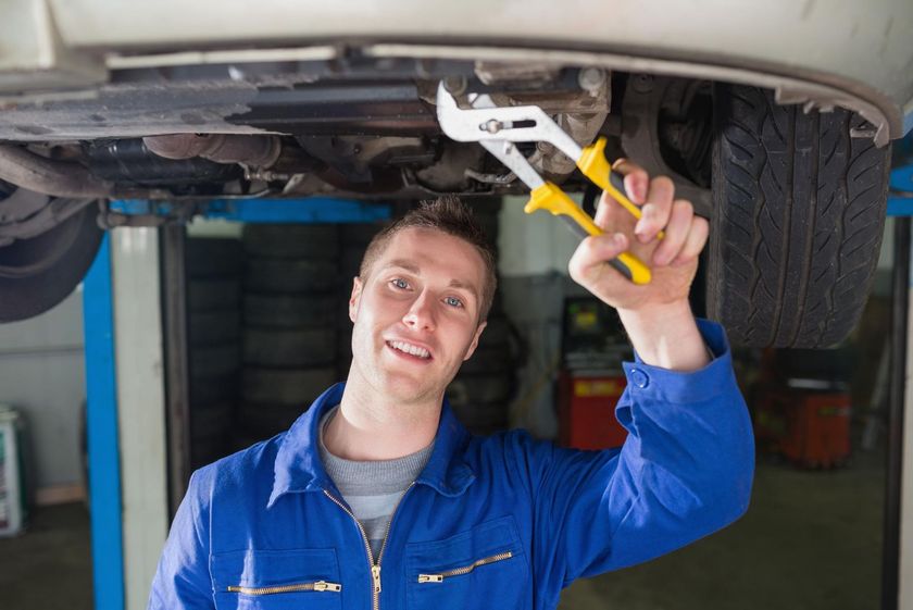Mechanic in blue coveralls using pliers to work under a car on a lift
