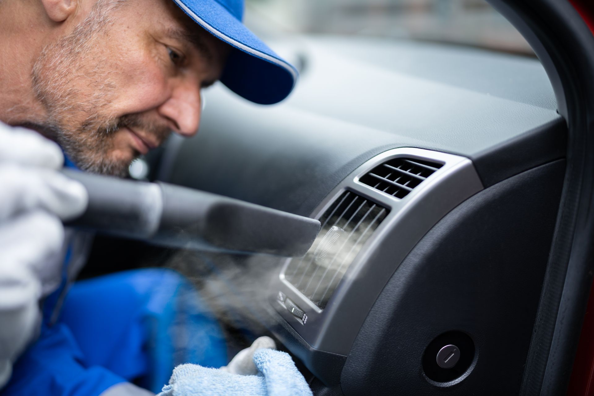 Mechanic cleaning car dashboard air vent with a brush and steam cleaner