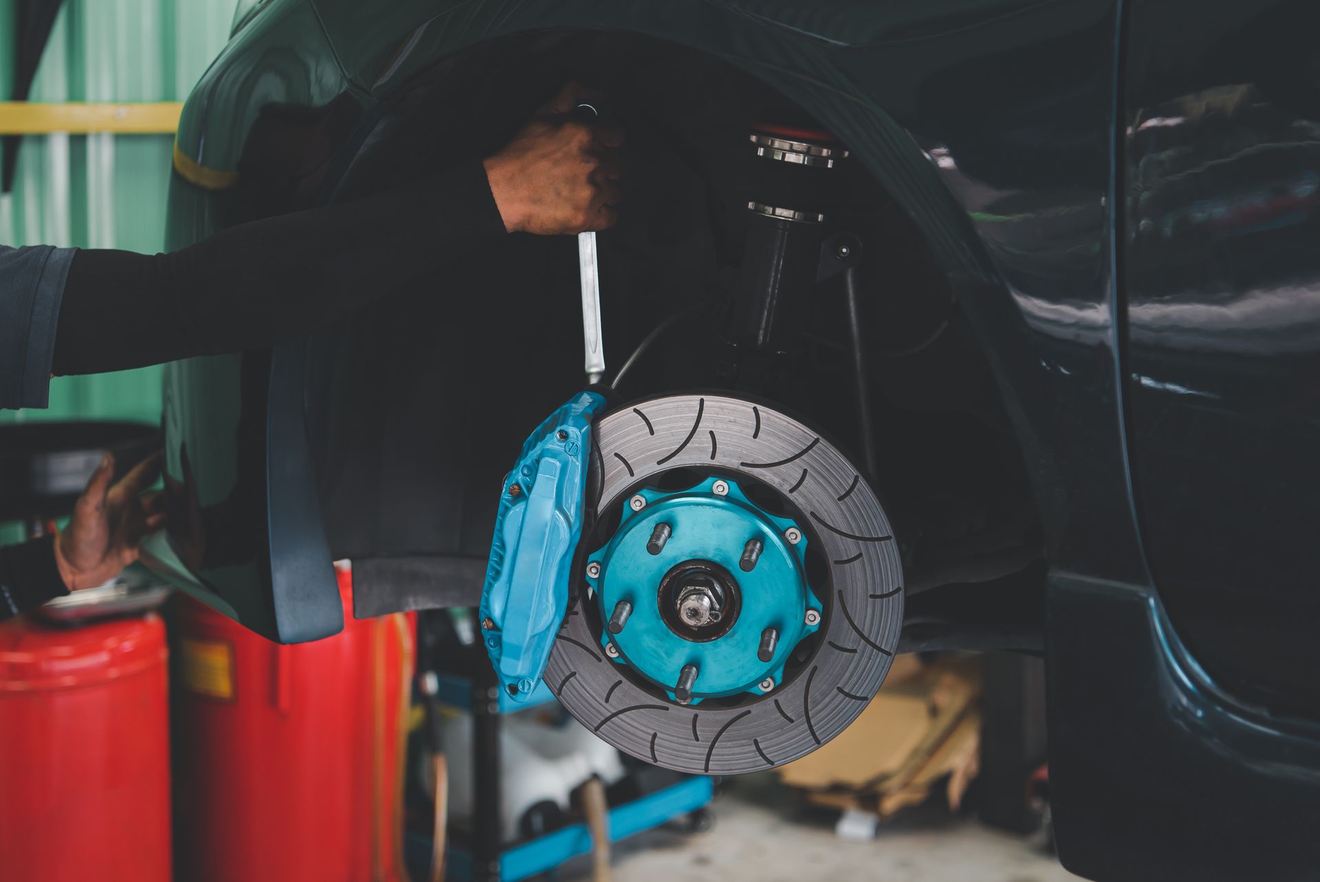Front car wheel with blue brake caliper and disc visible inside a garage