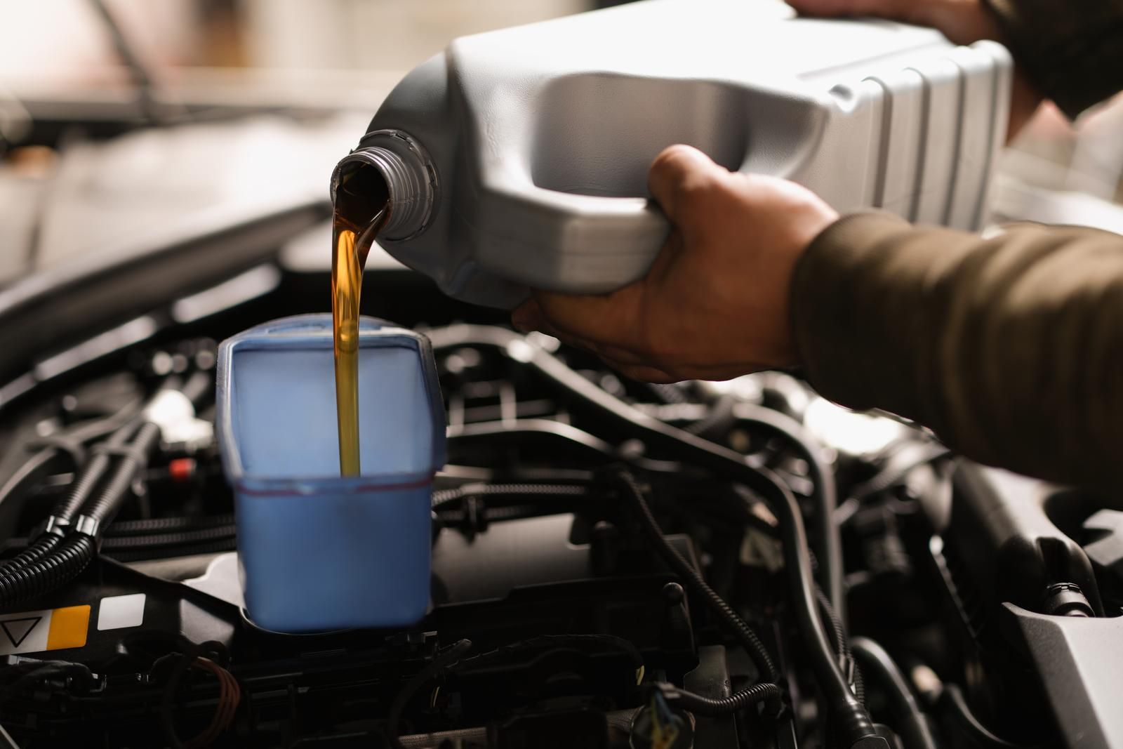 Pouring motor oil into a car engine with a blue container
