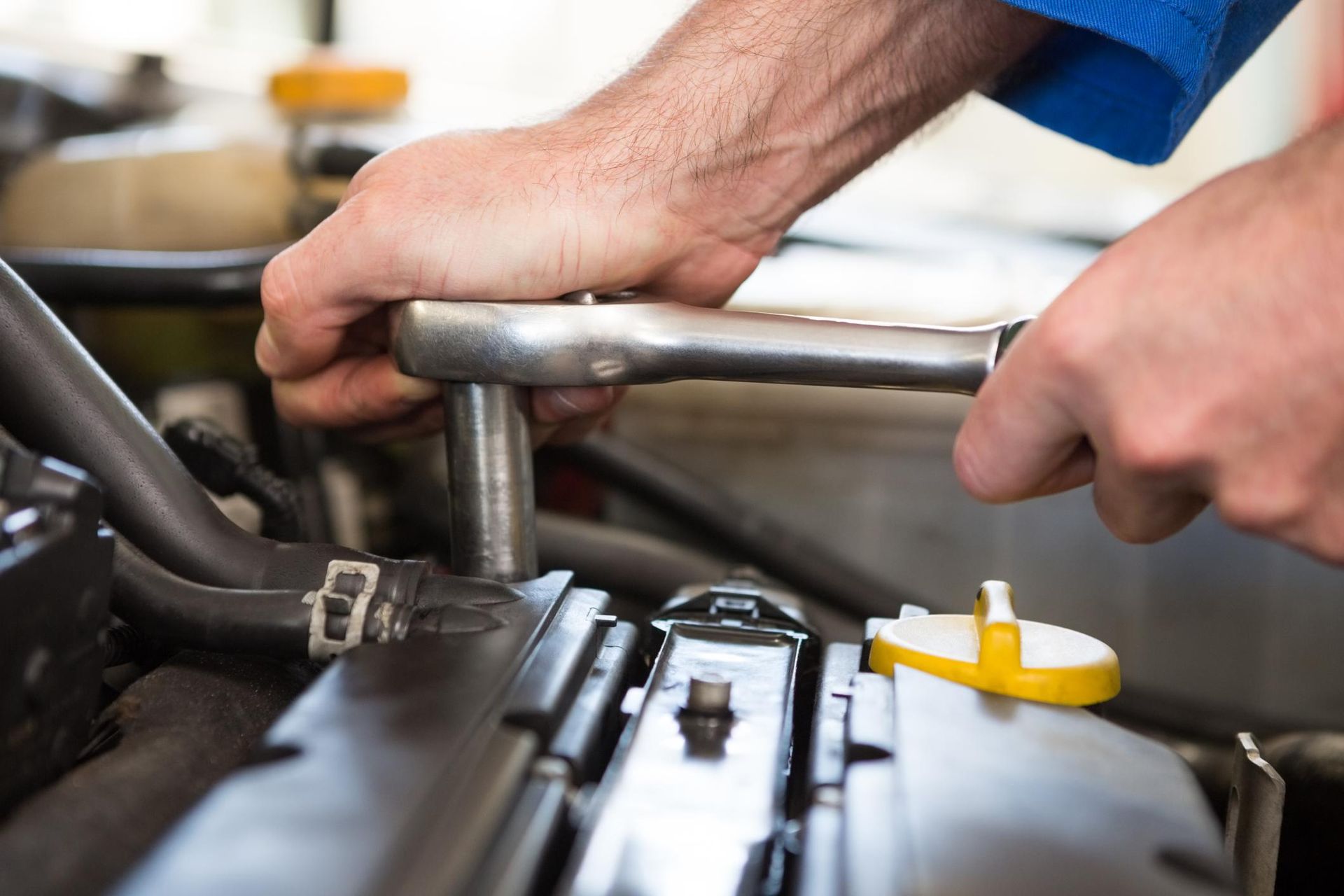 Hands using a wrench to work on a car engine in a garage