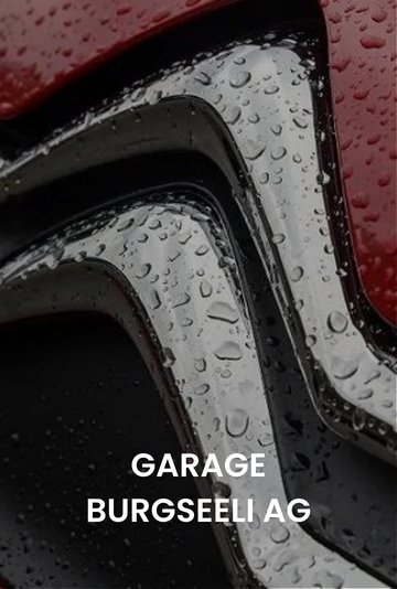 Nahaufnahme eines rot-schwarzen Autoemblems mit der Aufschrift „GARAGE BURGSELLAG“ bei Regenwetter