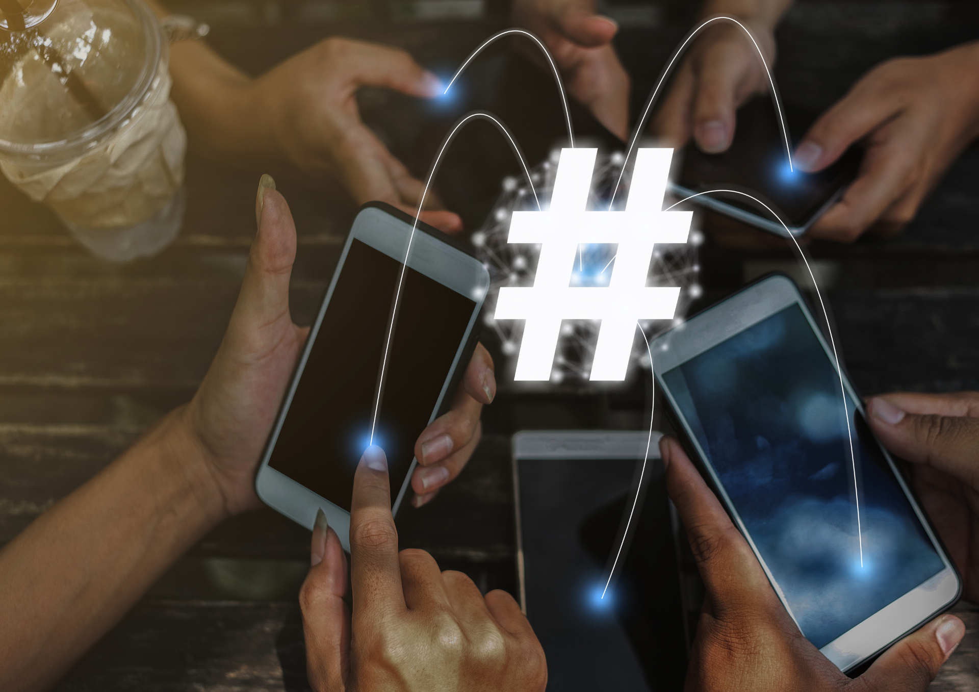 Des mains utilisant des smartphones autour d'un symbole hashtag lumineux sur une table