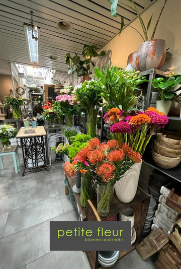 Ein Gang im Blumenladen mit farbenfrohen Sträußen und Grünpflanzen, darunter orange und rosa Blumen in weißen Vasen.