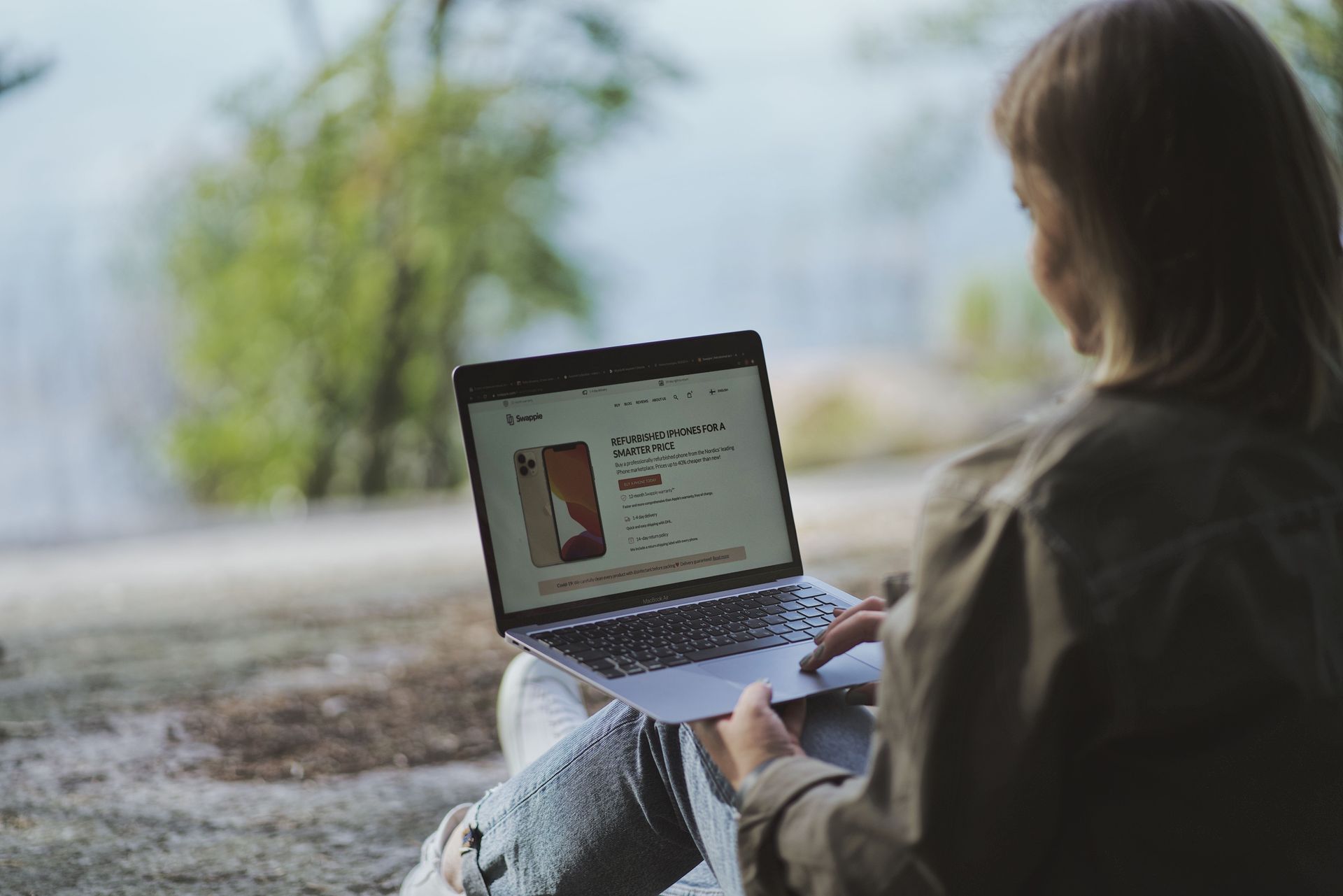 Person using a laptop outdoors, viewing a webpage on the screen.