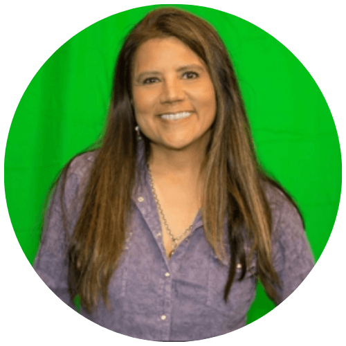 A smiling person with long brown hair wearing a buttoned purple shirt against a green screen background.