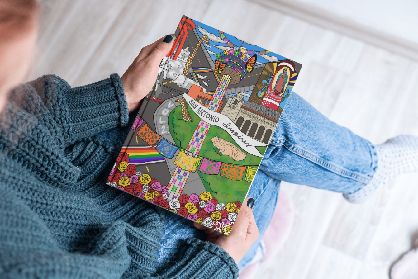 A person in a blue sweater and jeans holds a book with a vibrant, illustrated cover featuring diverse figures and patterns.