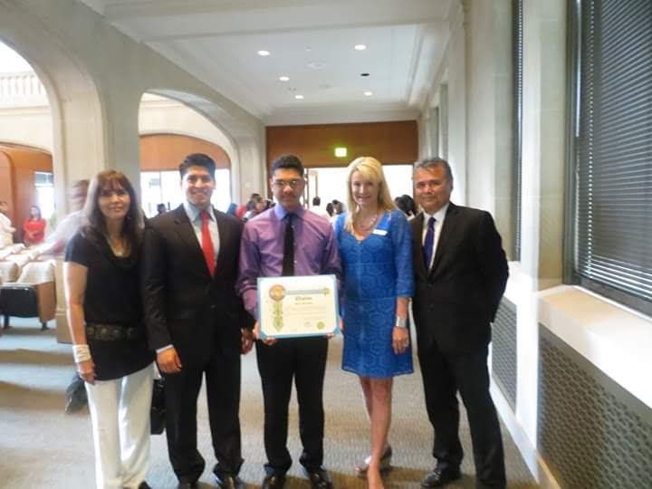 Five people standing in a hallway, with the person in the center holding a certificate.