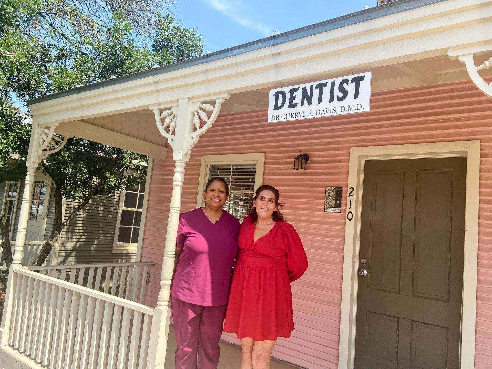 Two people stand on the porch of a pink building with a