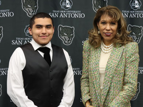 A young man in a vest and tie stands with a woman in a tweed blazer before a Texas A&M University-San Antonio backdrop.