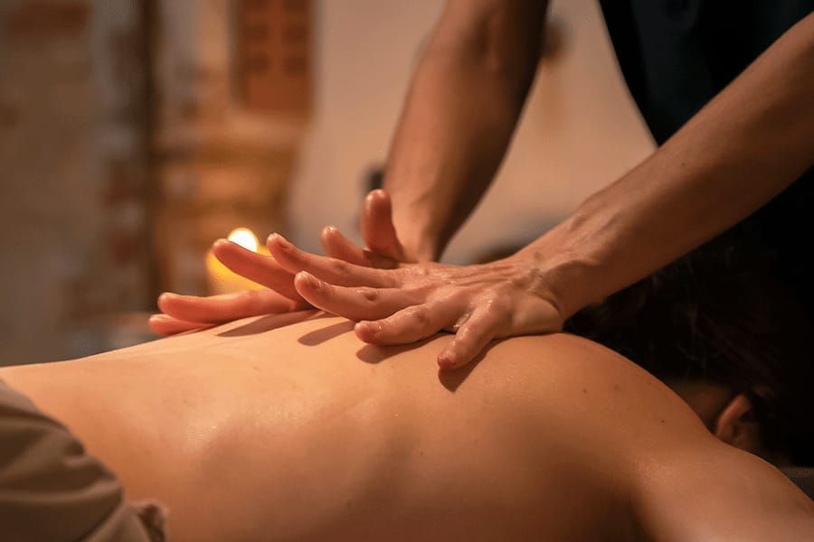 Persona recibiendo un masaje de espalda; manos del terapeuta aplicando presión en la espalda; habitación poco iluminada con una vela.
