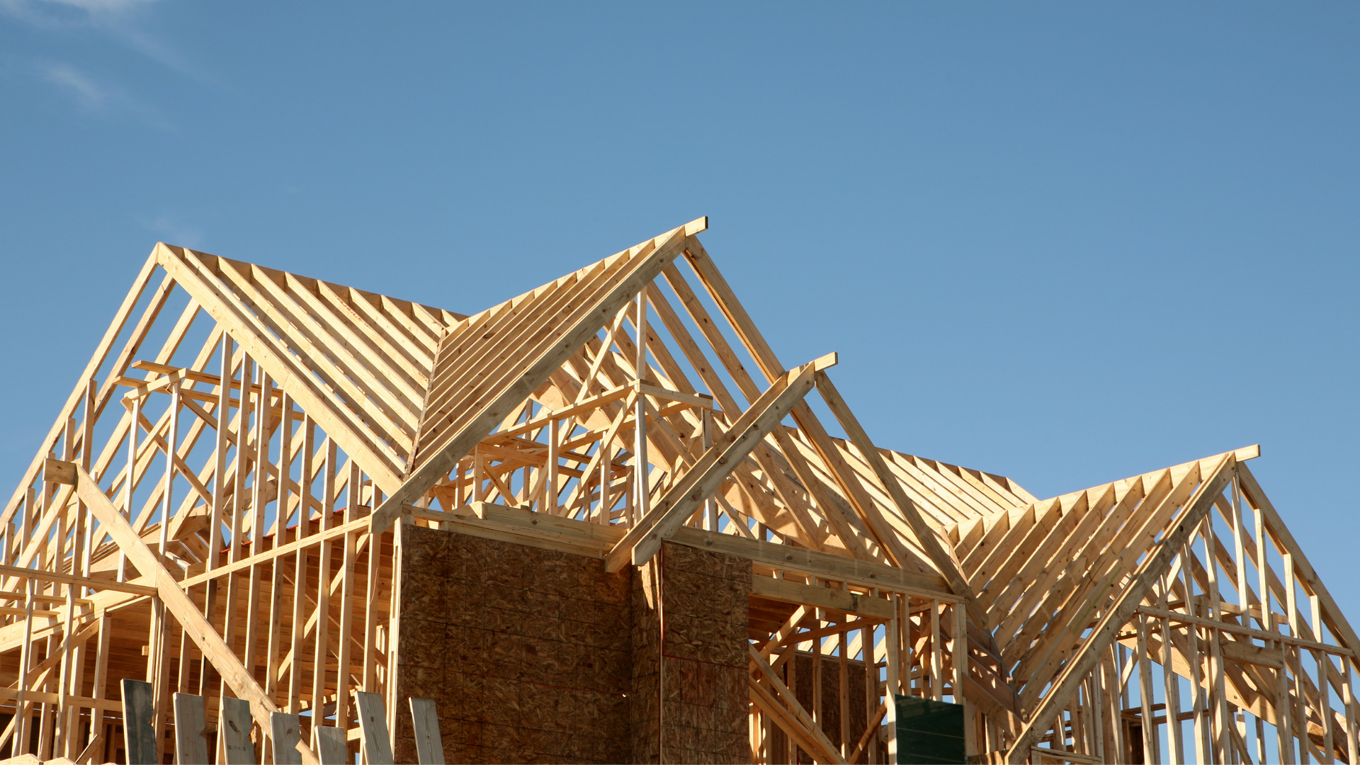 A wooden framework of a house under construction against a clear blue sky.