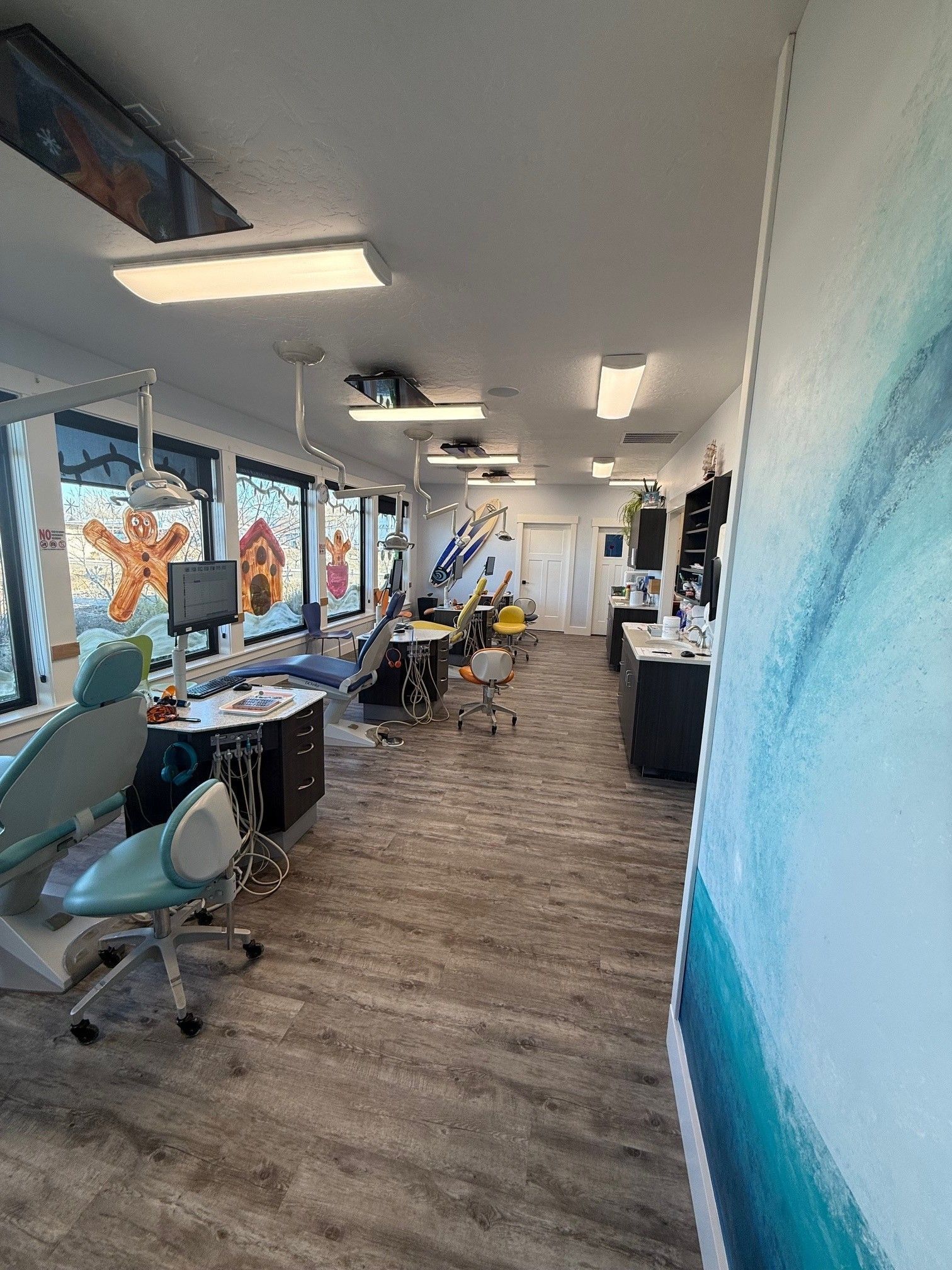 A bright, open-plan dental office with multiple chairs, light-colored flooring, and large windows with festive decorations.