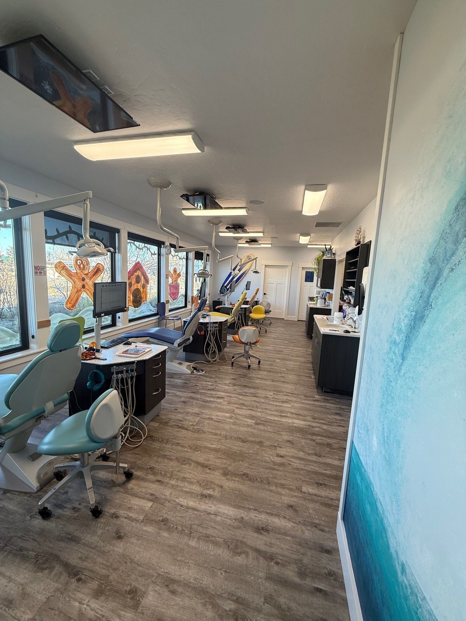A dental office with several patient chairs, equipment, and a mural on the right wall, set in a bright, modern room.