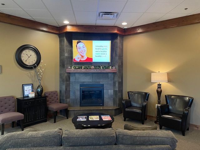 A seating area with a sofa, two armchairs, a fireplace with a mounted television, and a round table.