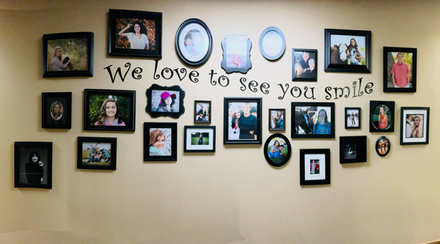 A beige wall featuring a collage of various framed photos surrounding the text