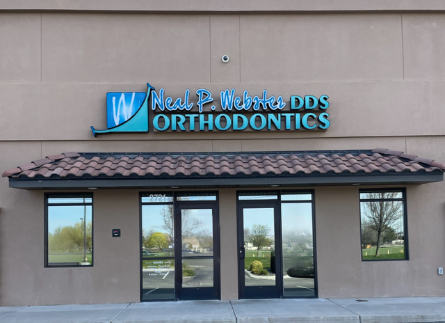 The storefront of Neal P. Webster DDS Orthodontics featuring a blue logo and lettering above two glass entry doors.