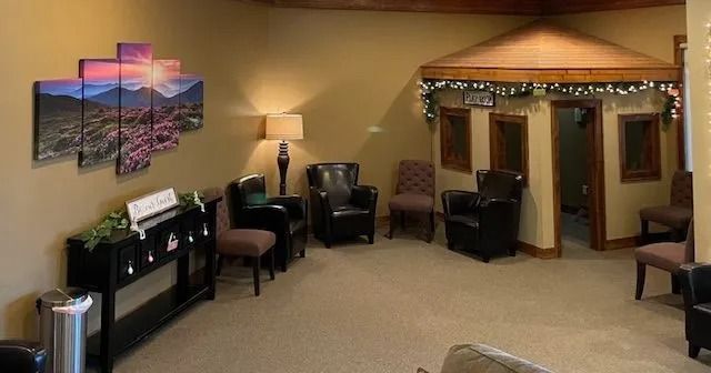 Waiting area with seating, artwork, and playhouse. Warm lighting, neutral walls, carpeted floor.