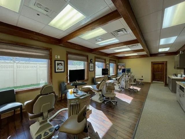 Dental office interior with patient chairs, windows, wood beams, and dental equipment.
