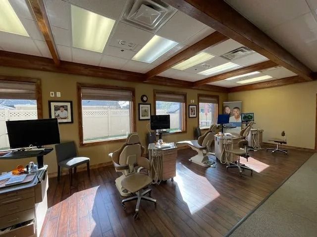 Dental office interior with chairs, windows, and monitors; brown wood beams.