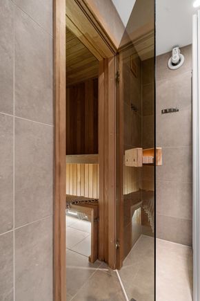 Open sauna door with wood interior and tiled walls in a modern bathroom.