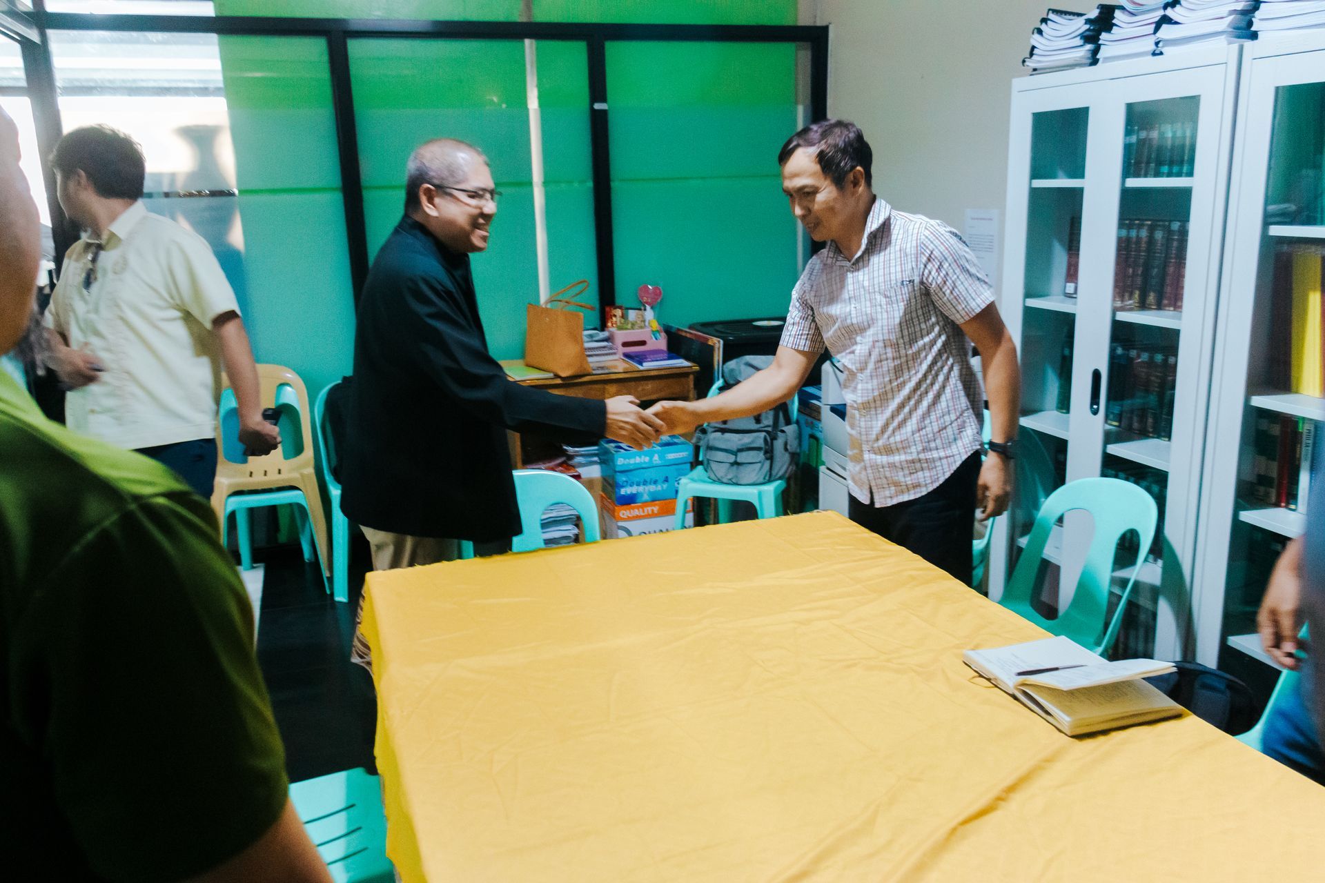 Two representatives shake hands across a table during a community engagement meeting under Project Caraga.