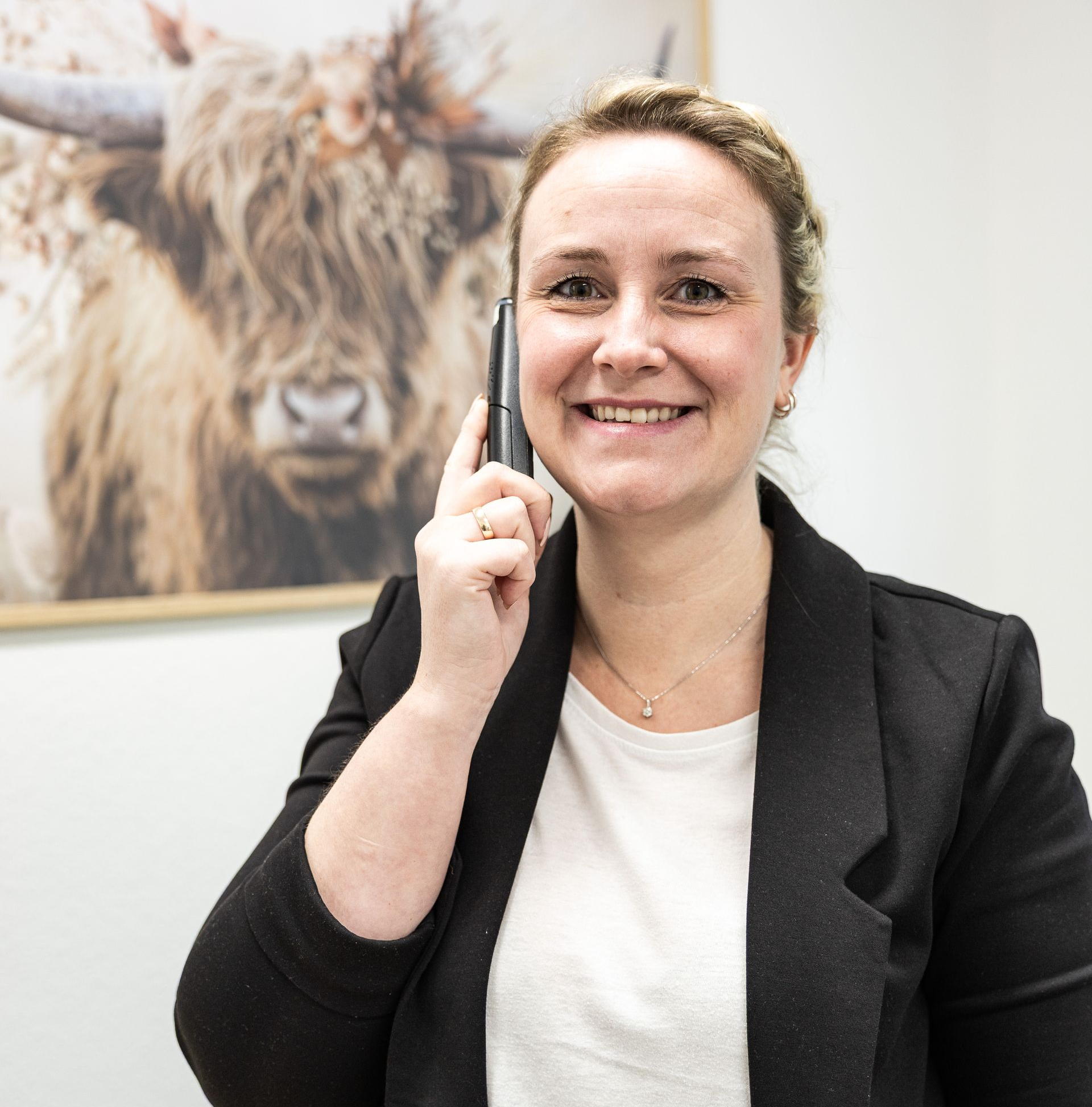 Frau im Blazer telefoniert, lächelt. An der Wand hängt ein Stierbild.