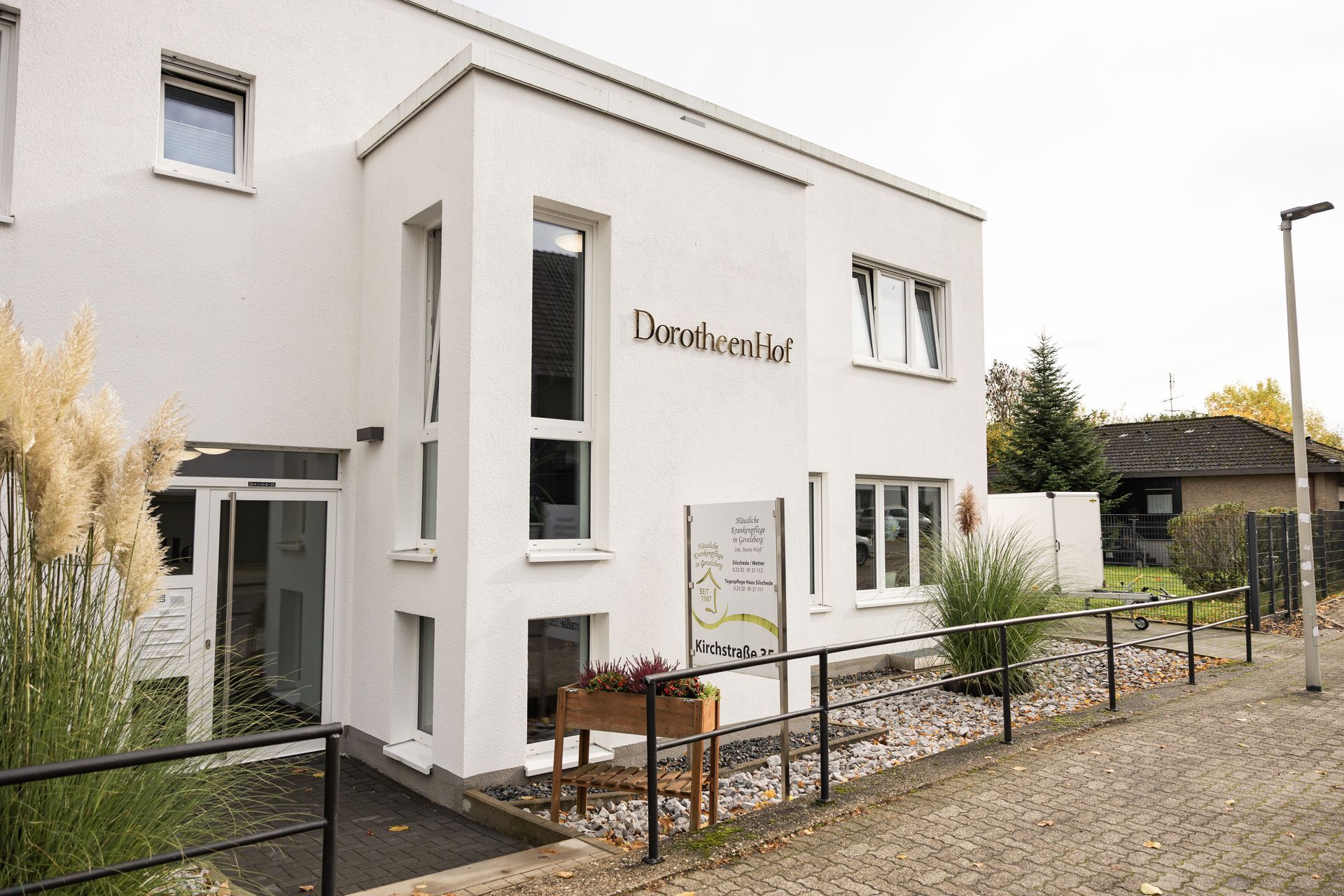 Weißes Gebäude, Schild „Dorchen Hof“, Auffahrtsrampe. Straße, Pflanzen, bedeckter Himmel.