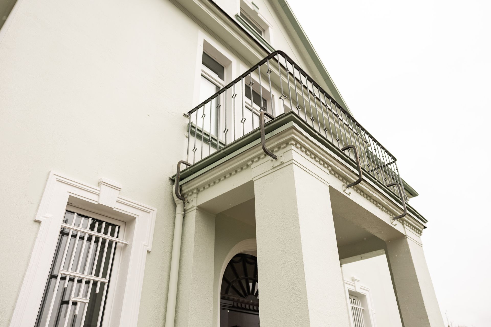 Weißes Gebäude mit Balkon und Bogeneingang, aus niedriger Perspektive an einem bewölkten Tag betrachtet.
