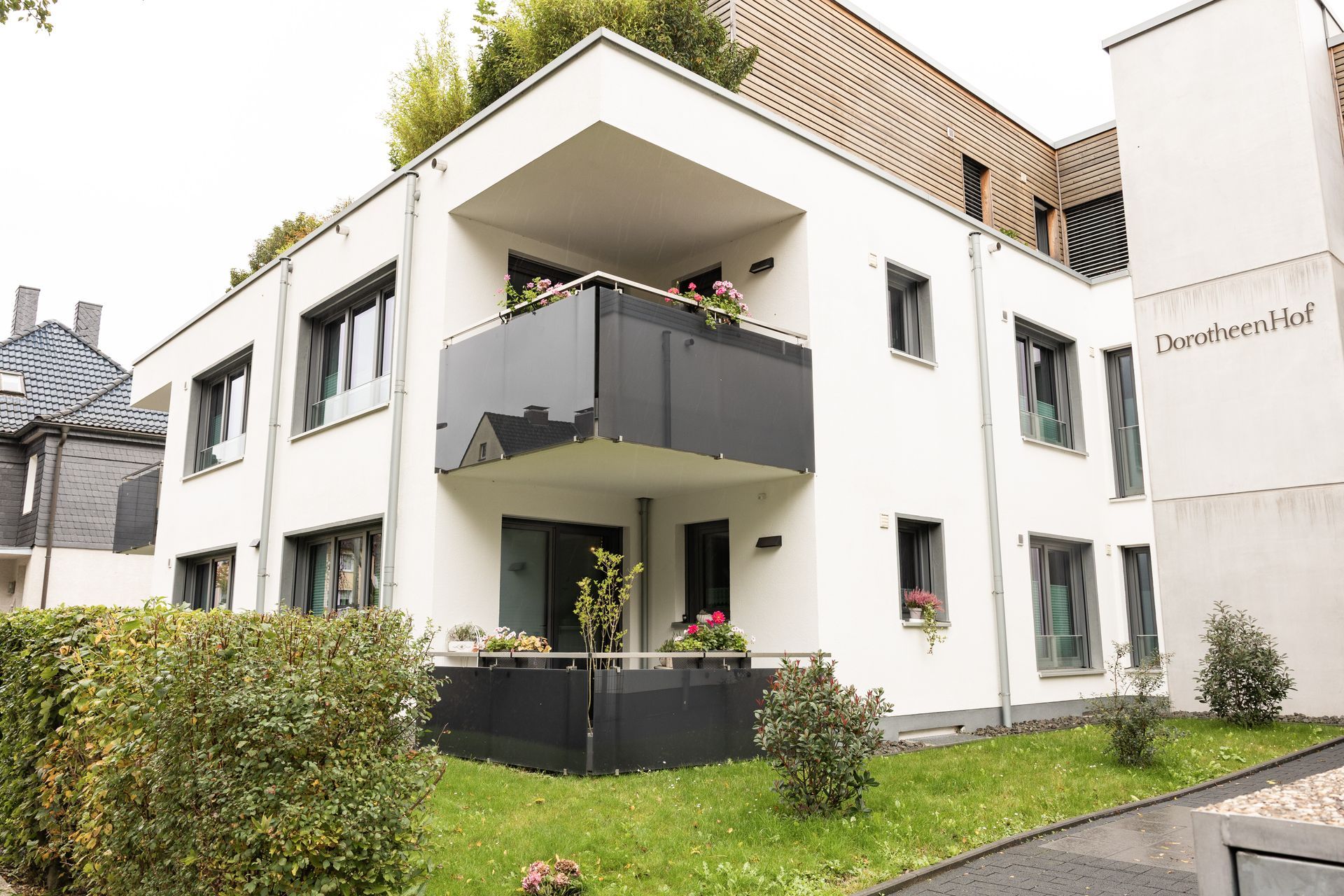 Weißes, modernes Apartmentgebäude mit Balkonen und Grünanlagen.