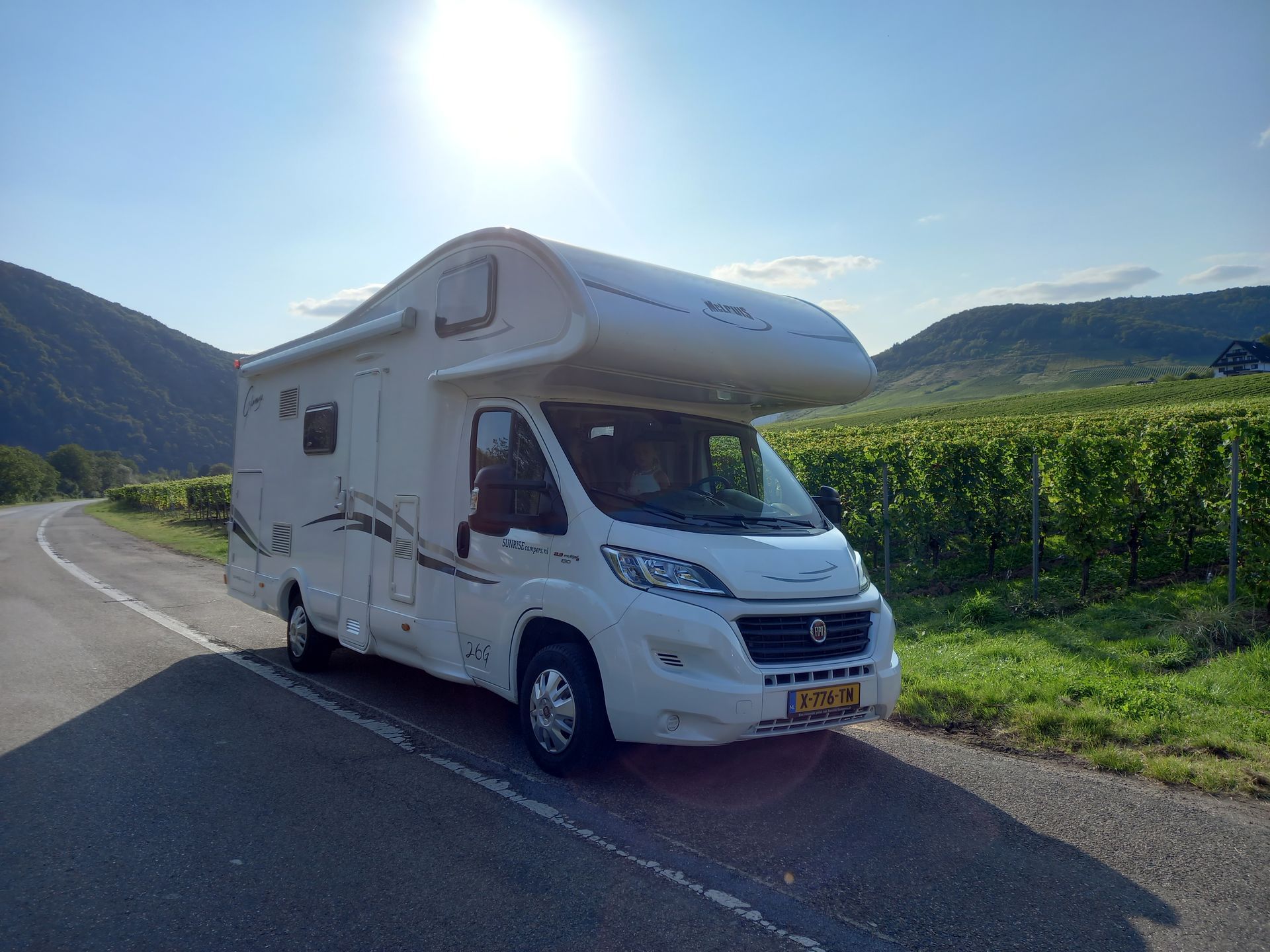 Camper Lars geparkeerd op een weg naast een wijngaard, zonnige dag, bergen op de achtergrond.