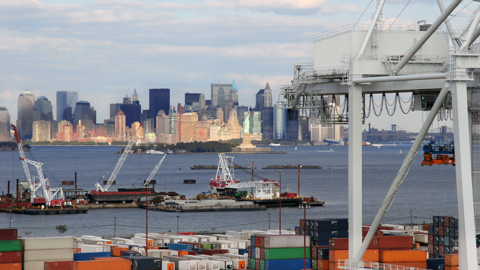 Harbor cranes and barges in the foreground with Manhattan skyline across the water at dusk