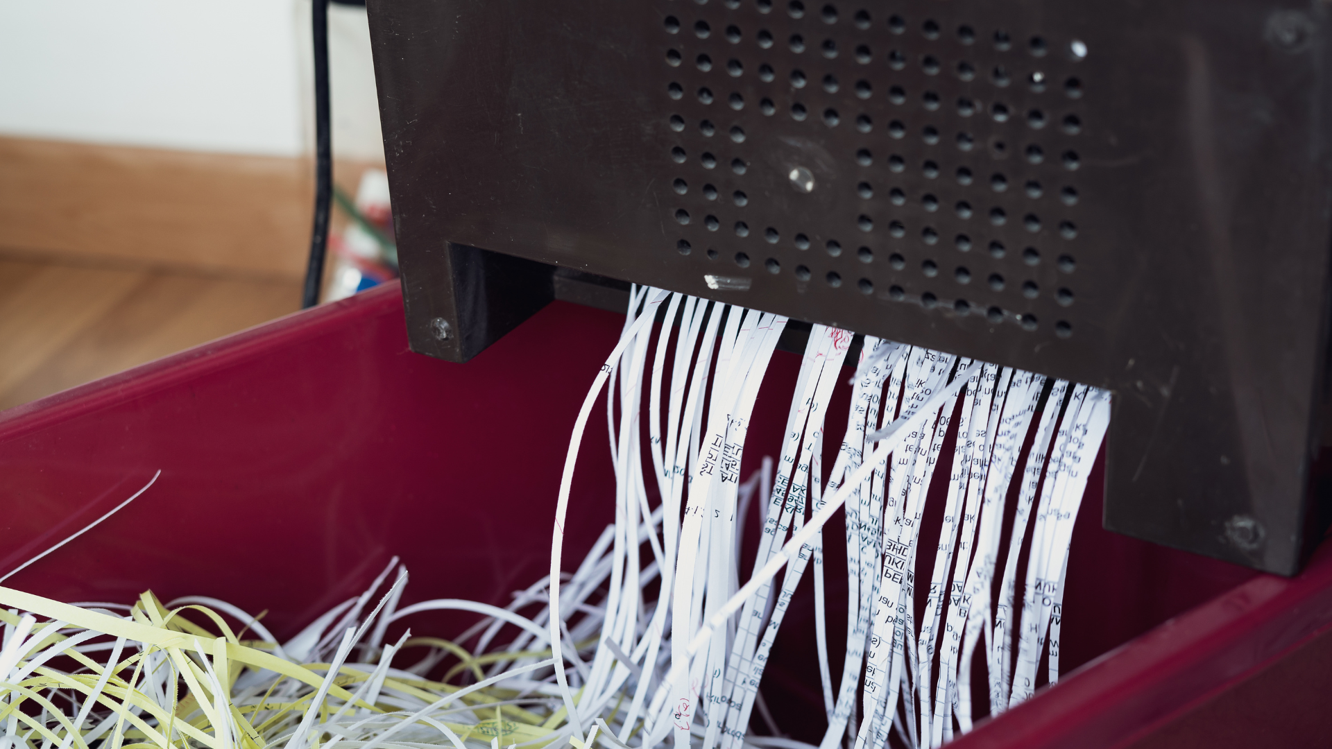 Paper strips being cut from a black shredder into a red bin.
