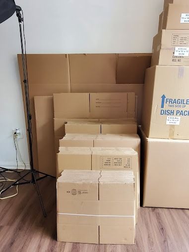 Stacked cardboard shipping boxes in a room beside a microphone stand and cables
