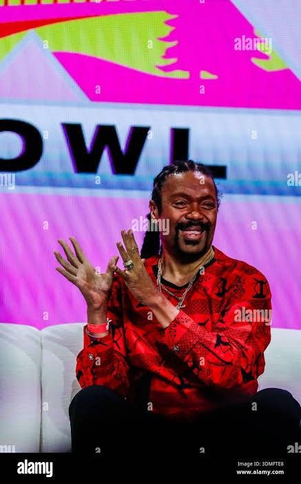 Man in a red shirt clapping on stage before a white and pink backdrop