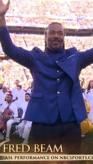 Fred Beam in a blue jacket raises both arms at a crowded outdoor event.