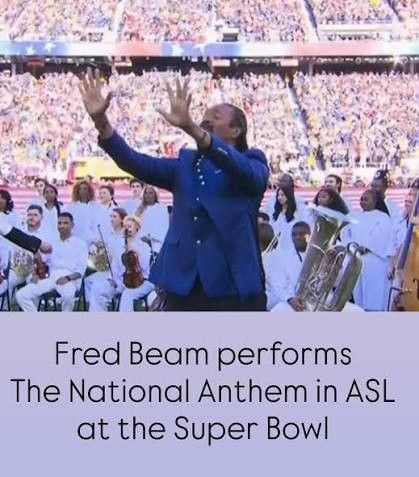 Fred Beam signing the National Anthem in blue suit at the Super Bowl, stadium crowd behind him