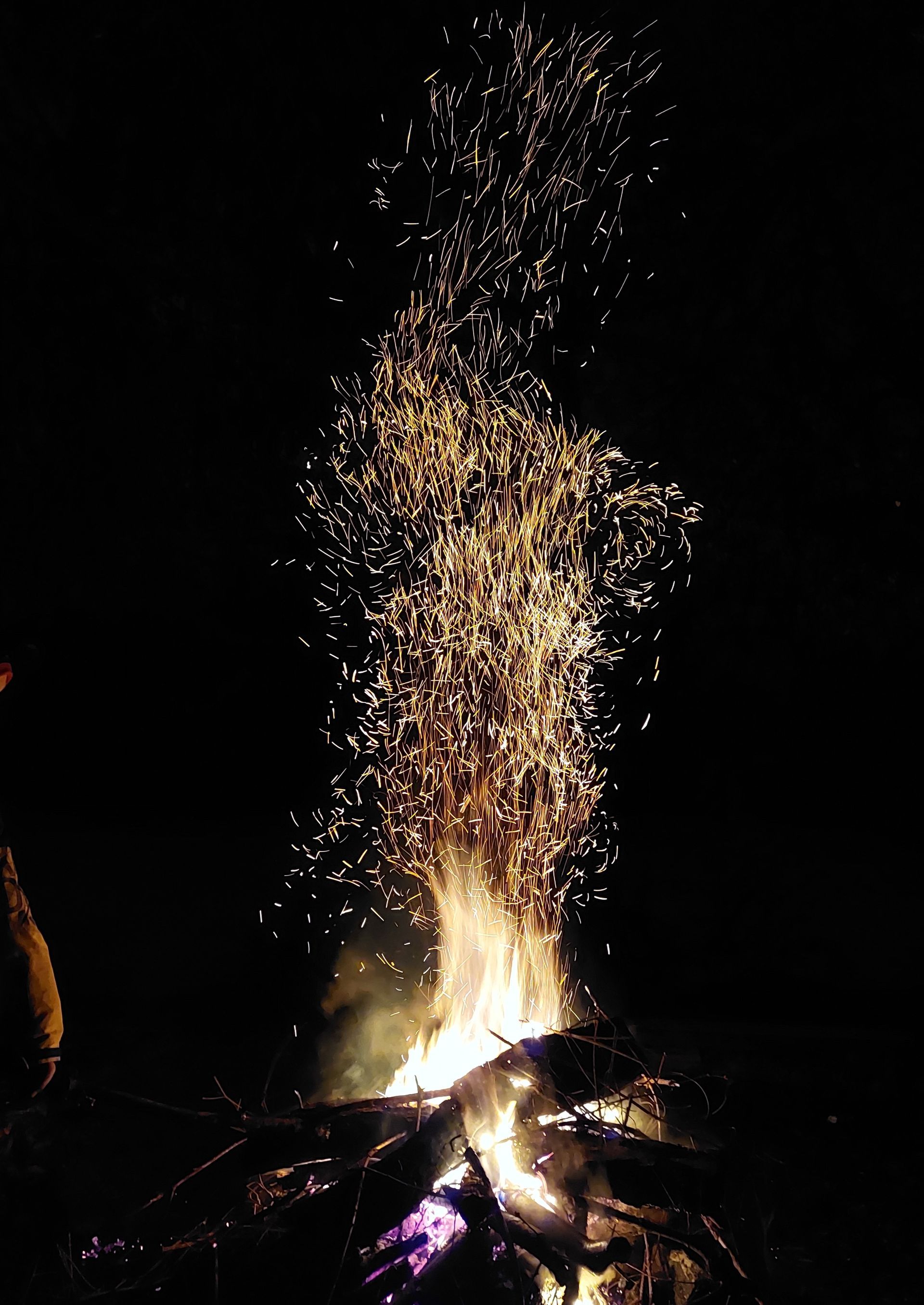 Ein helles Feuer brennt, Funken sprühen vor dunklem Hintergrund.
