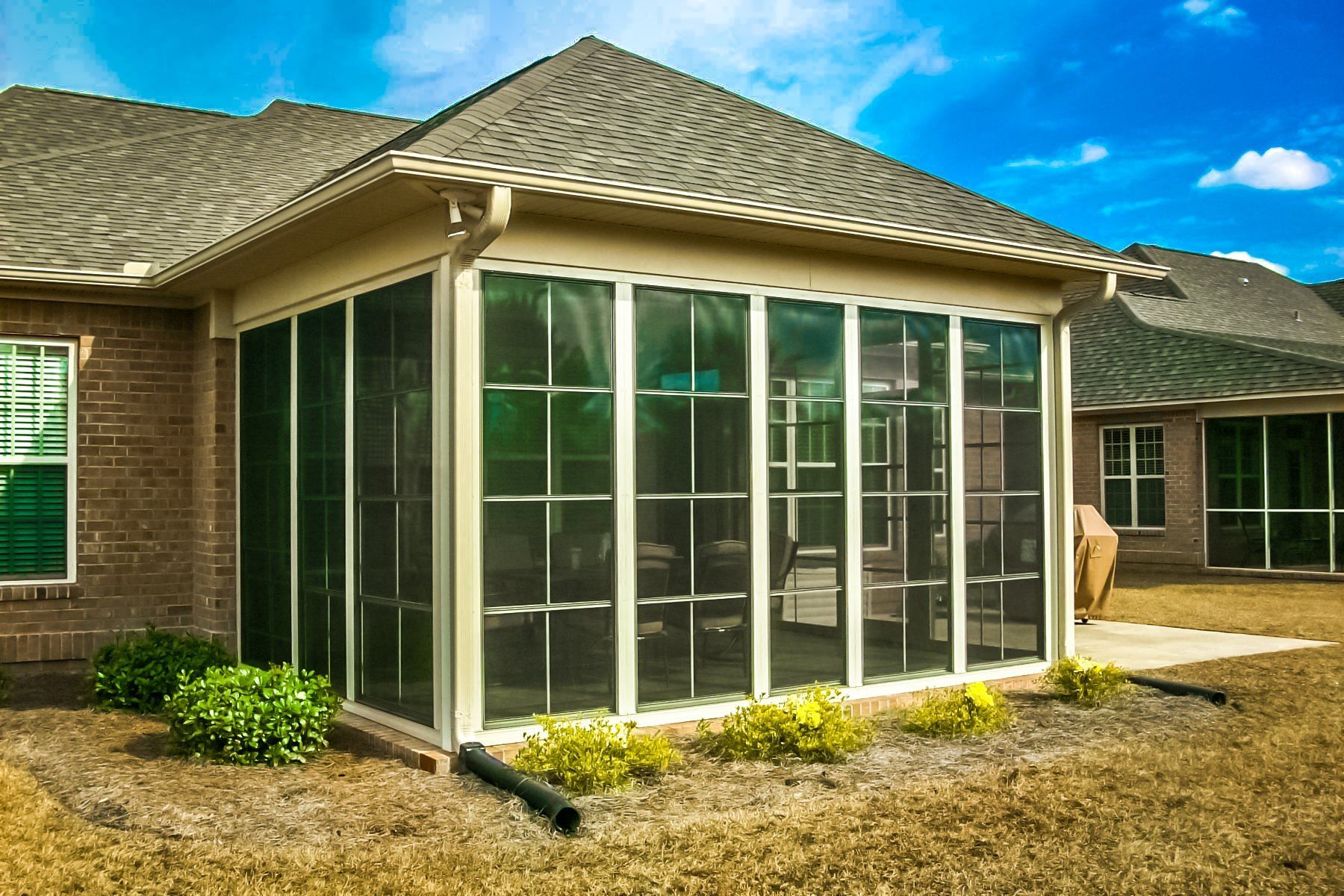 Screened patio on a brick house with white-framed windows and a tiled roof under a bright blue sky