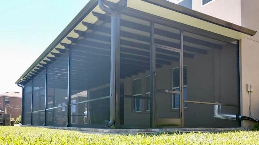 Modern dark-wood house porch with a sloped roof and screened walls in bright sunlight