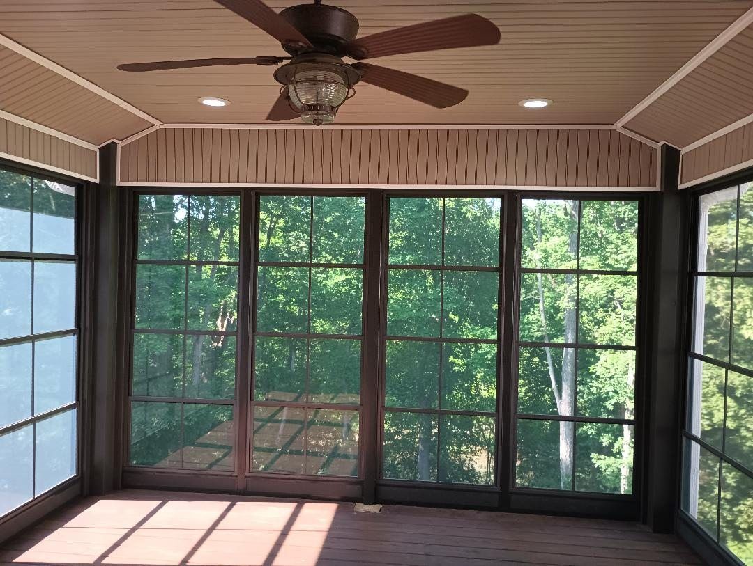 Screened porch with ceiling fan, large windows, and sunlight filtering onto the floor