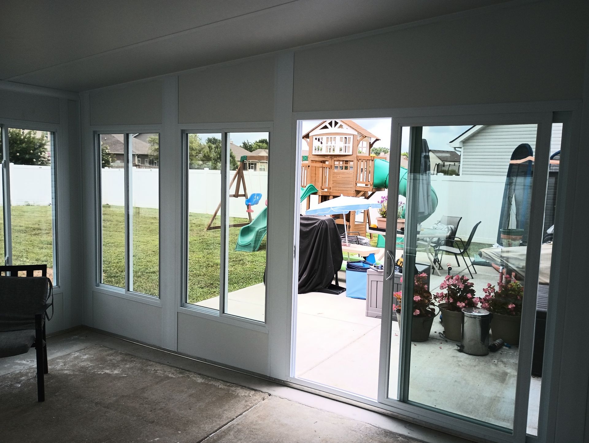 Covered patio with sliding glass doors, a playset outside, and potted flowers near the entrance.