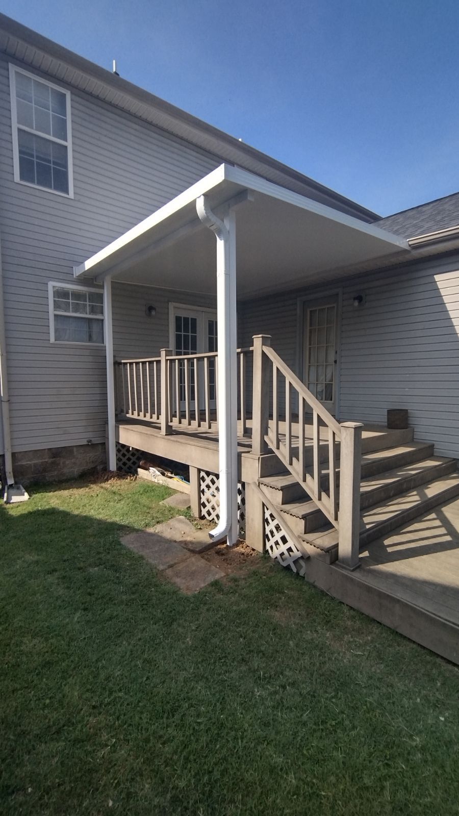 Small beige house side entrance with white covered porch, wooden steps, railing, and wheelchair ramp access