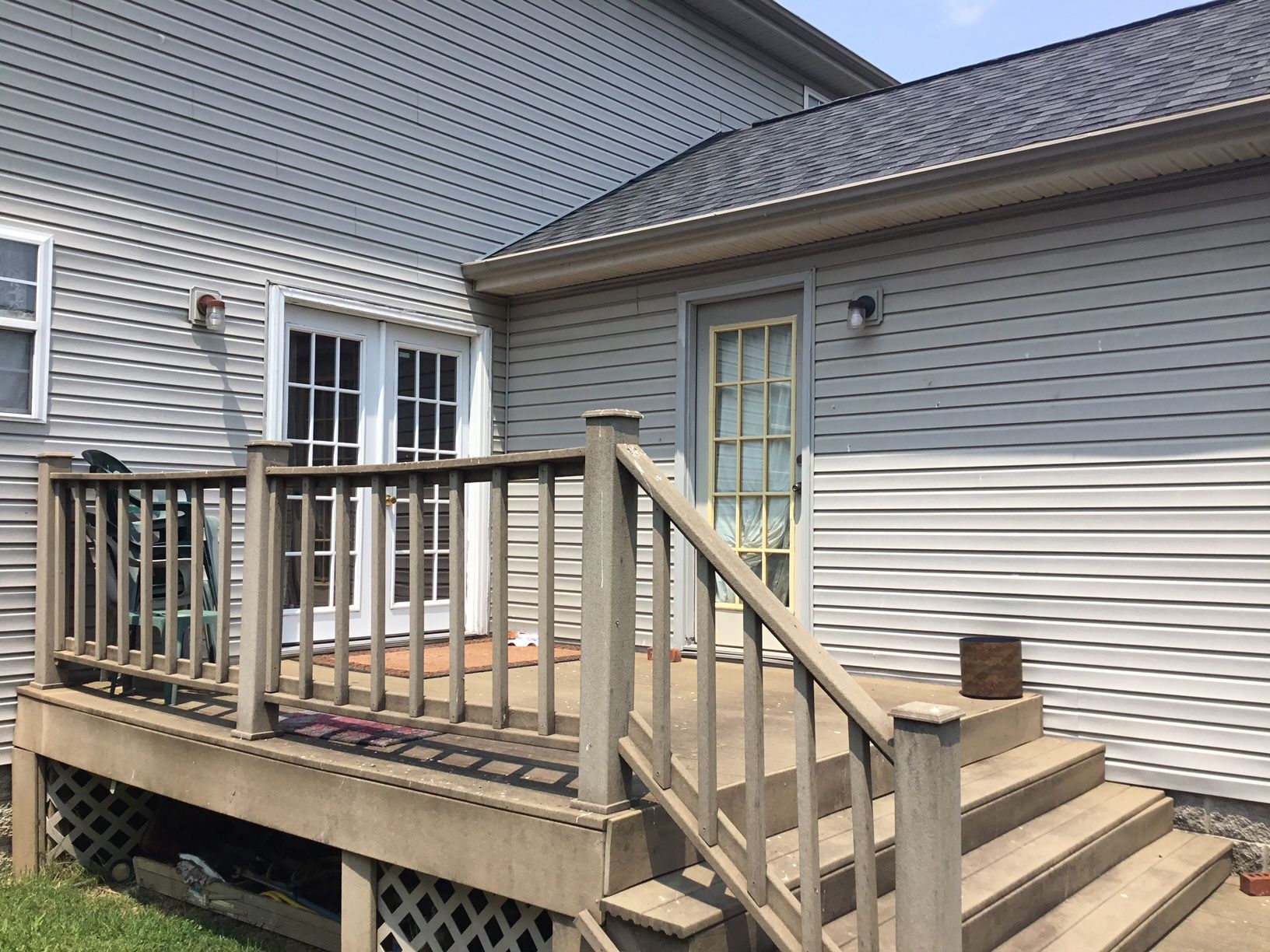 Wooden backyard deck with stairs and railing beside a gray house and patio door