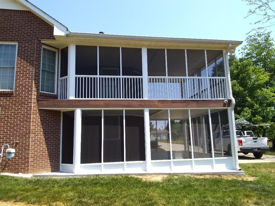 Two-story brick house with screened porch and white railing, viewed from the yard.